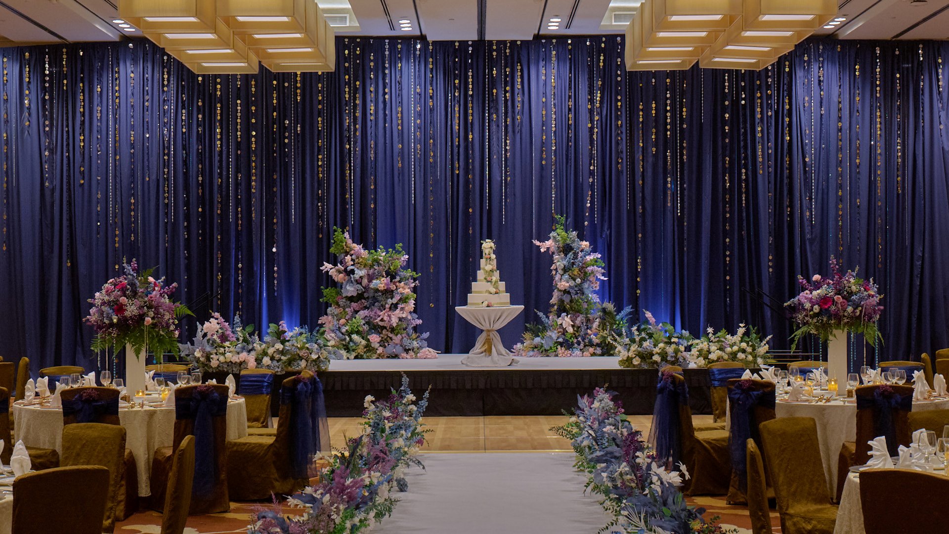 Panggung pernikahan dengan dekorasi bunga dan latar belakang biru yang elegan